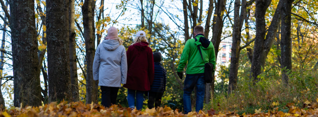 Nelihenkinen perhe kävelee syksyisessä puistossa.