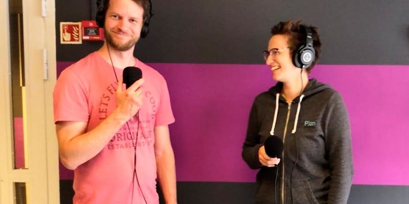 Mies ja nainen seisovat kuulokkeet korvillaan ja pitelevät käsissään mikrofonia.