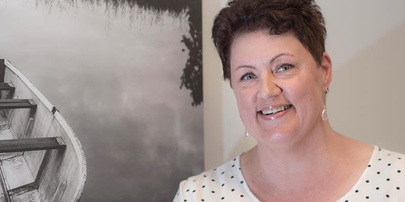 Nainen katsoo kameraan ja hymyilee.