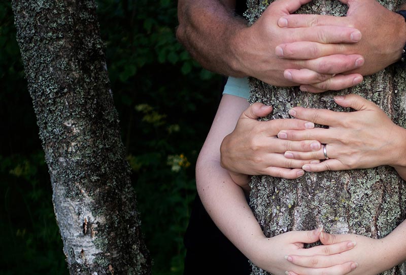 Kolme ihmistä halaavat yhdessä puun runkoa.