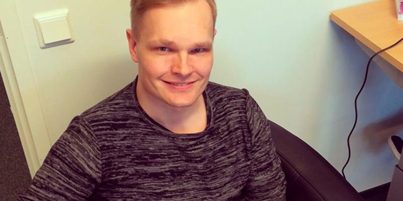 Mies istuu nojatuolilla ja hymyillen katsoo kameraan.