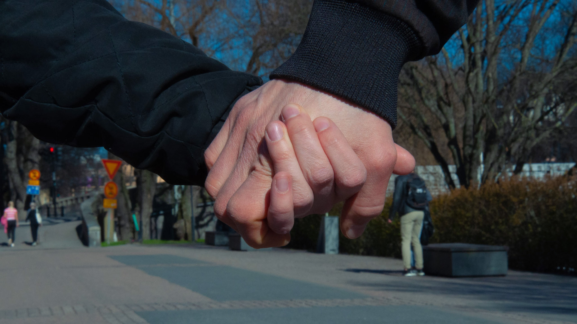 Kaksi henkilöä pitävät toisiaan kädestä ulkona. 