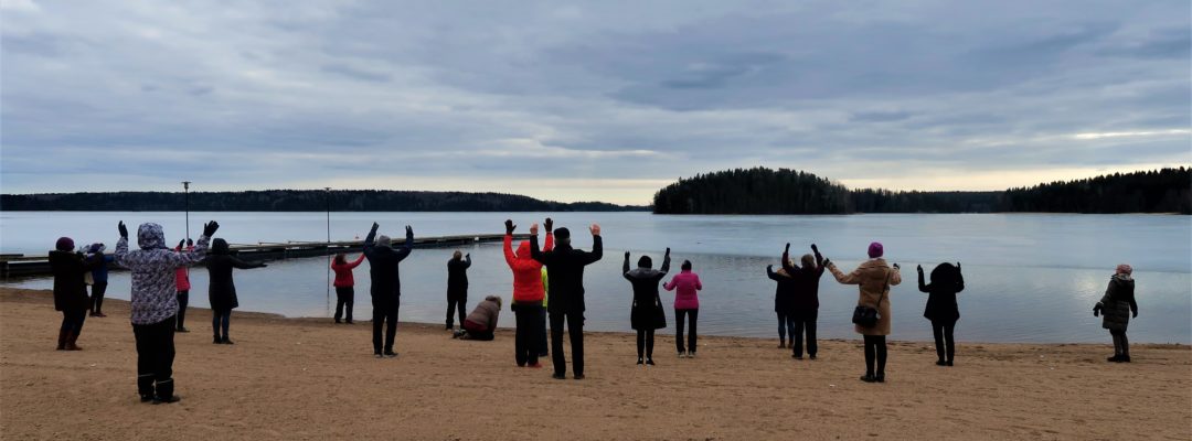 Useat ihmiset ovat hiekkarannalla ja pitelevät käsiä ylhäällä.