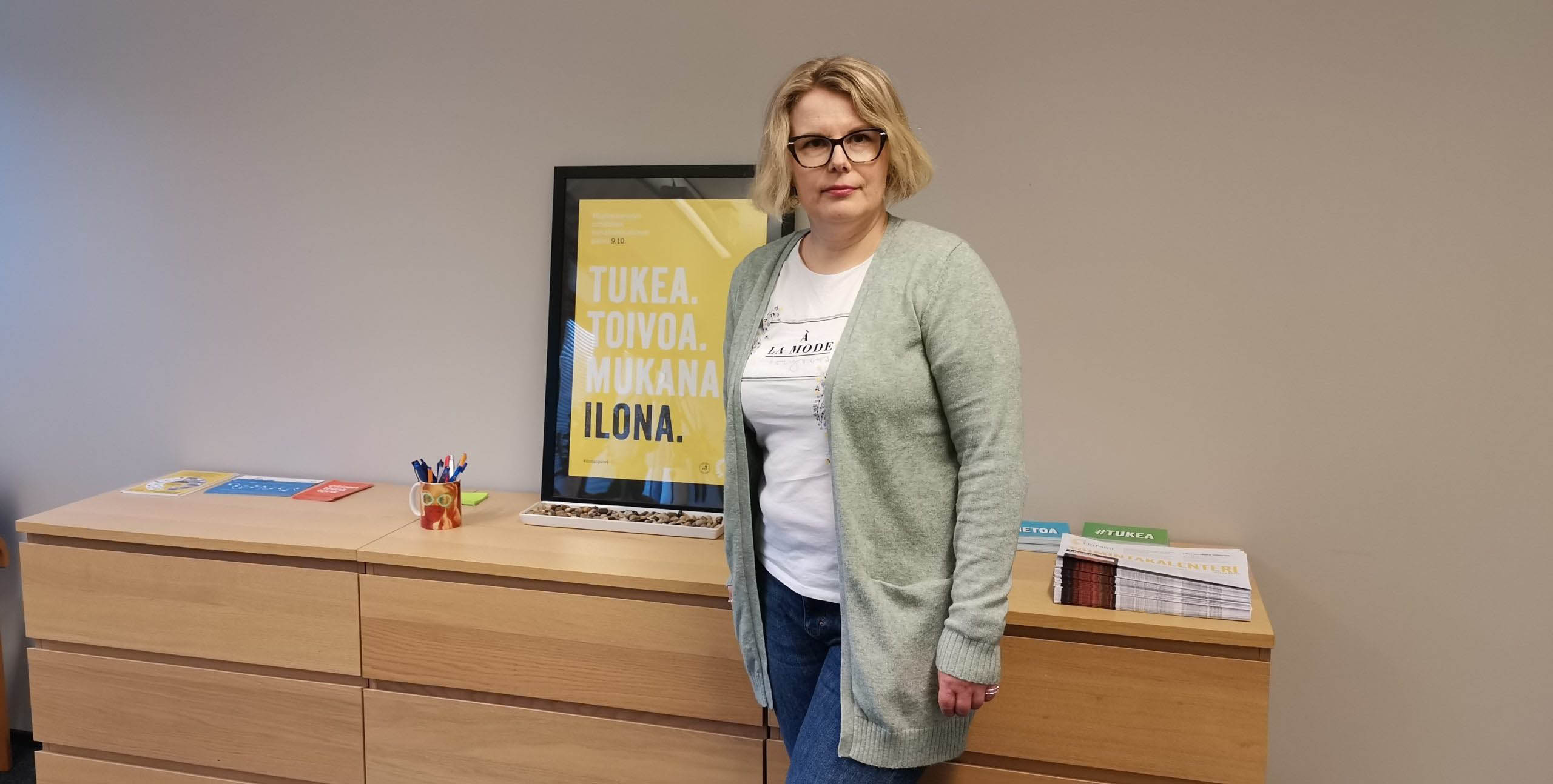 Nainen seisoo lipaston edessä ja katsoo kameraan.