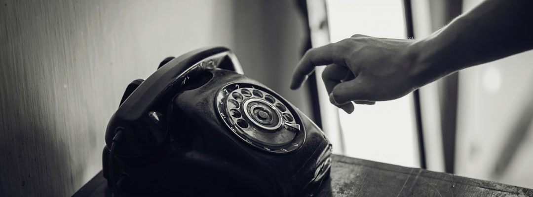 Henkilö on pyöräyttämässä lankapuhelimen pyöritettävää numeroiden valintalevyä.