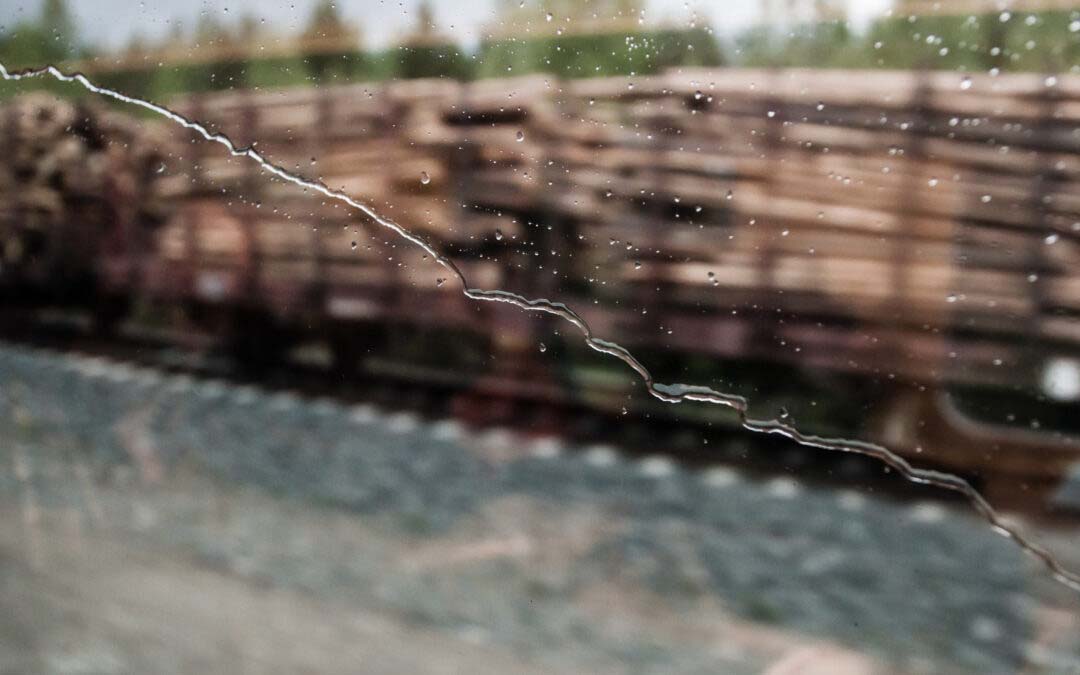 Sadepisaroiden kastaman junanikkunan takana tukkilastillinen tavarajunan vaunu.