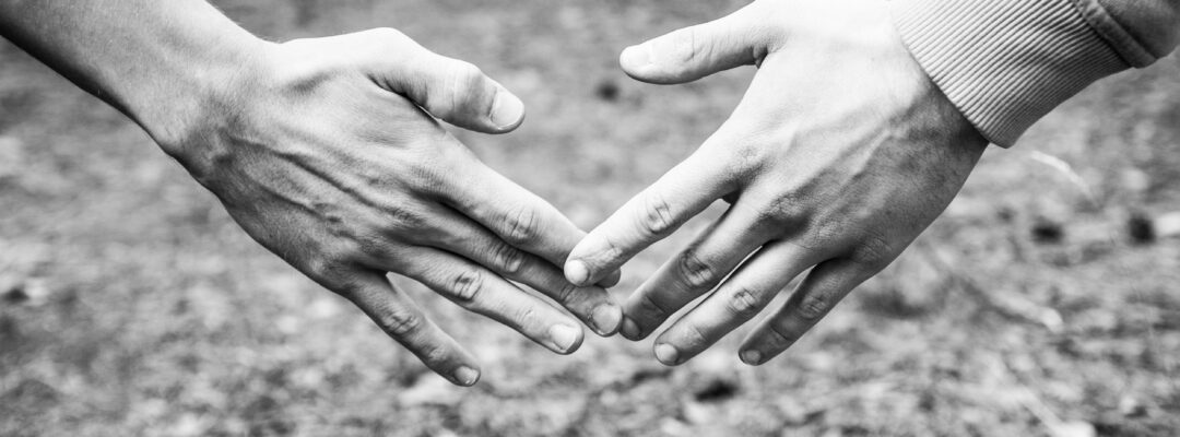 Kahden ihmisen vasemmat käden etu--ja keskisormet koskettavat toisiaan.