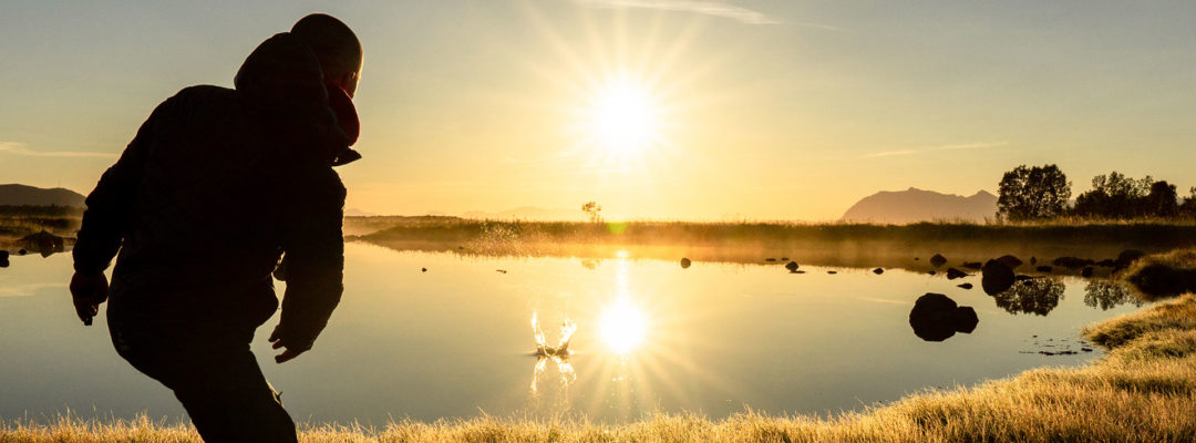 Henkilö heittää vesileipiä rannalla auringon paistaessa.