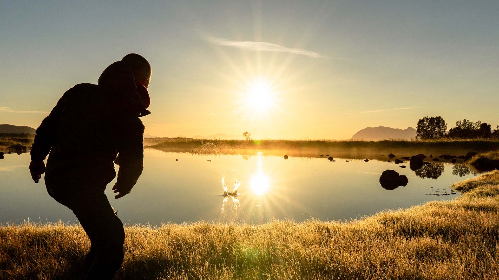 Henkilö heittää vesileipiä rannalla auringon paistaessa.