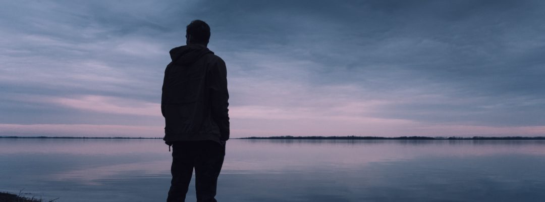 Henkilö seisoo rannalla. Taivas on tummansininen ja taivaanranta vaaleanpunertava.