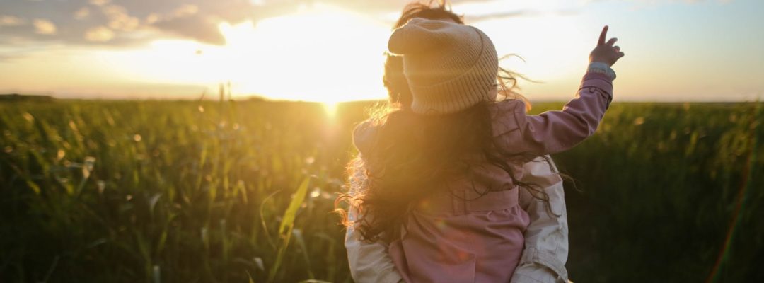 Henkilö seisoo pellolla ja pitää sylissä lasta.