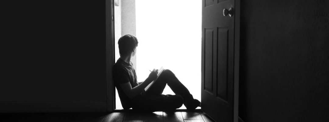 Poika istuu oven kynnyksellä ja katsoo ulos.