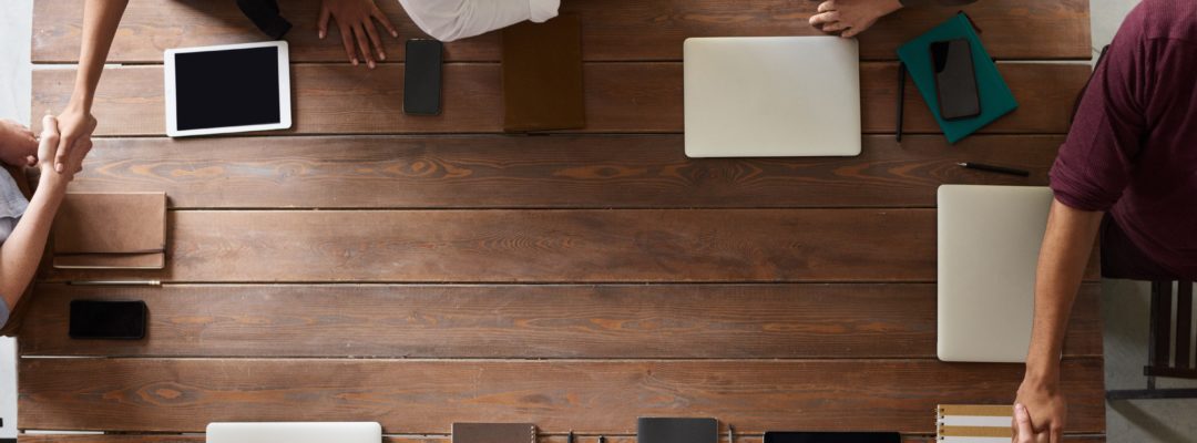 Ihmiset istuvat pöydän äärellä ja kättelevät toisiaan.